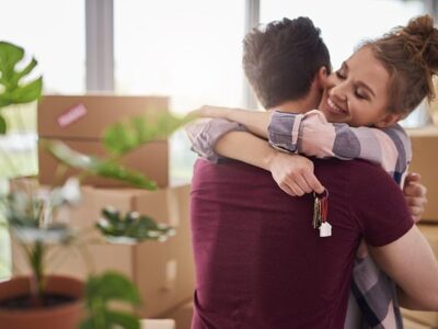 couple hugging in new home holding house keys with cardboard boxes behind